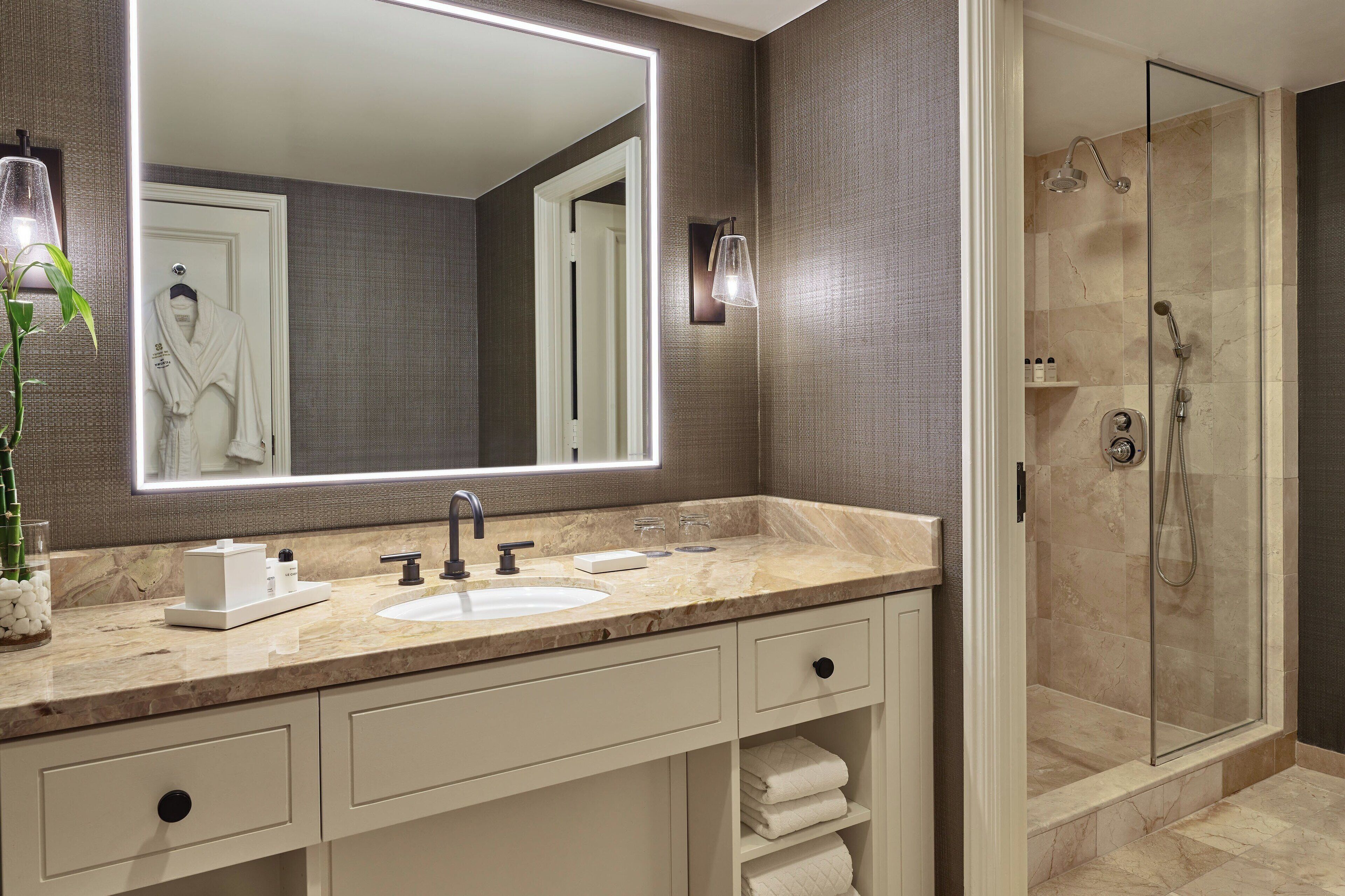 A modern bathroom with a large mirror, a sink, and a glass-enclosed shower.
