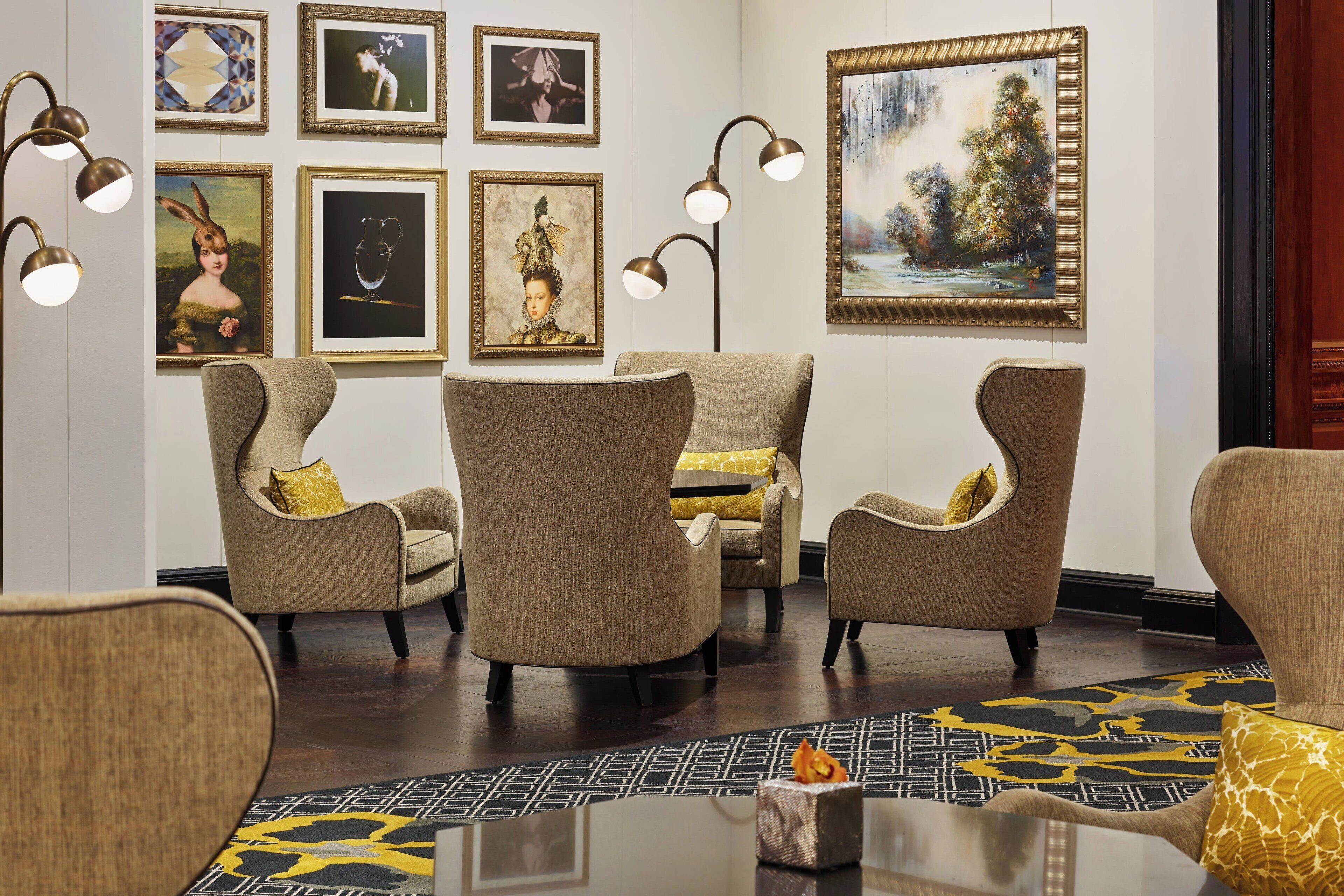 A room with four armchairs, a coffee table, and a floor lamp. There are framed artworks on the wall and a large painting above the armchairs.