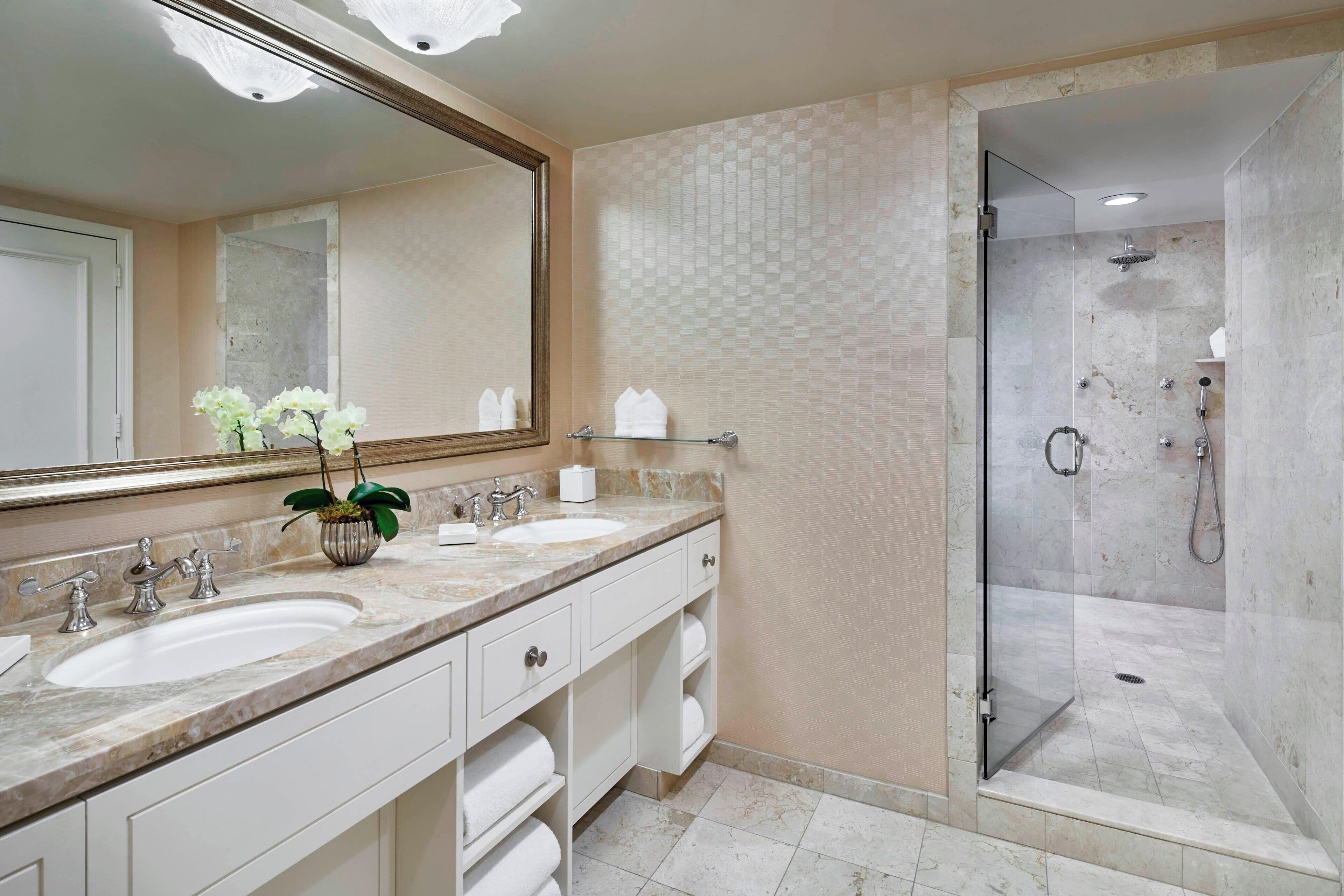 A bathroom with two sinks, a large mirror, a shower with a glass door, and a potted plant.