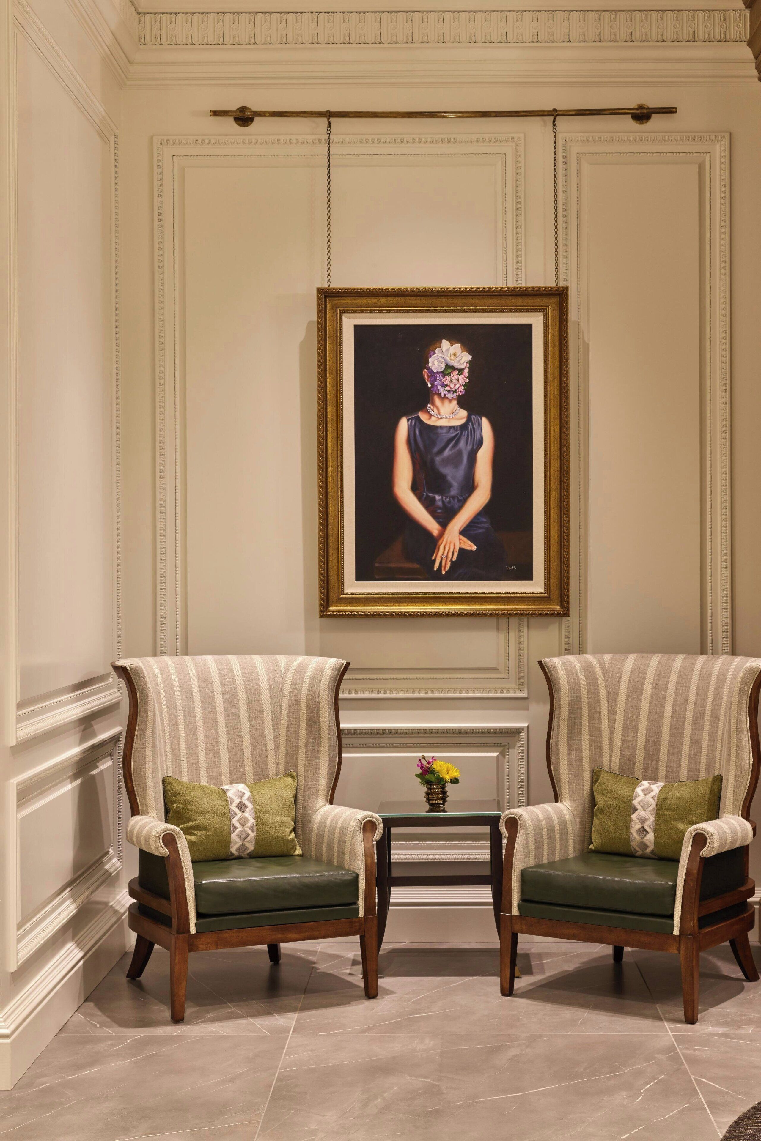 Two armchairs with striped upholstery and green cushions, a framed portrait on the wall, and a small vase with flowers on a table between them.
