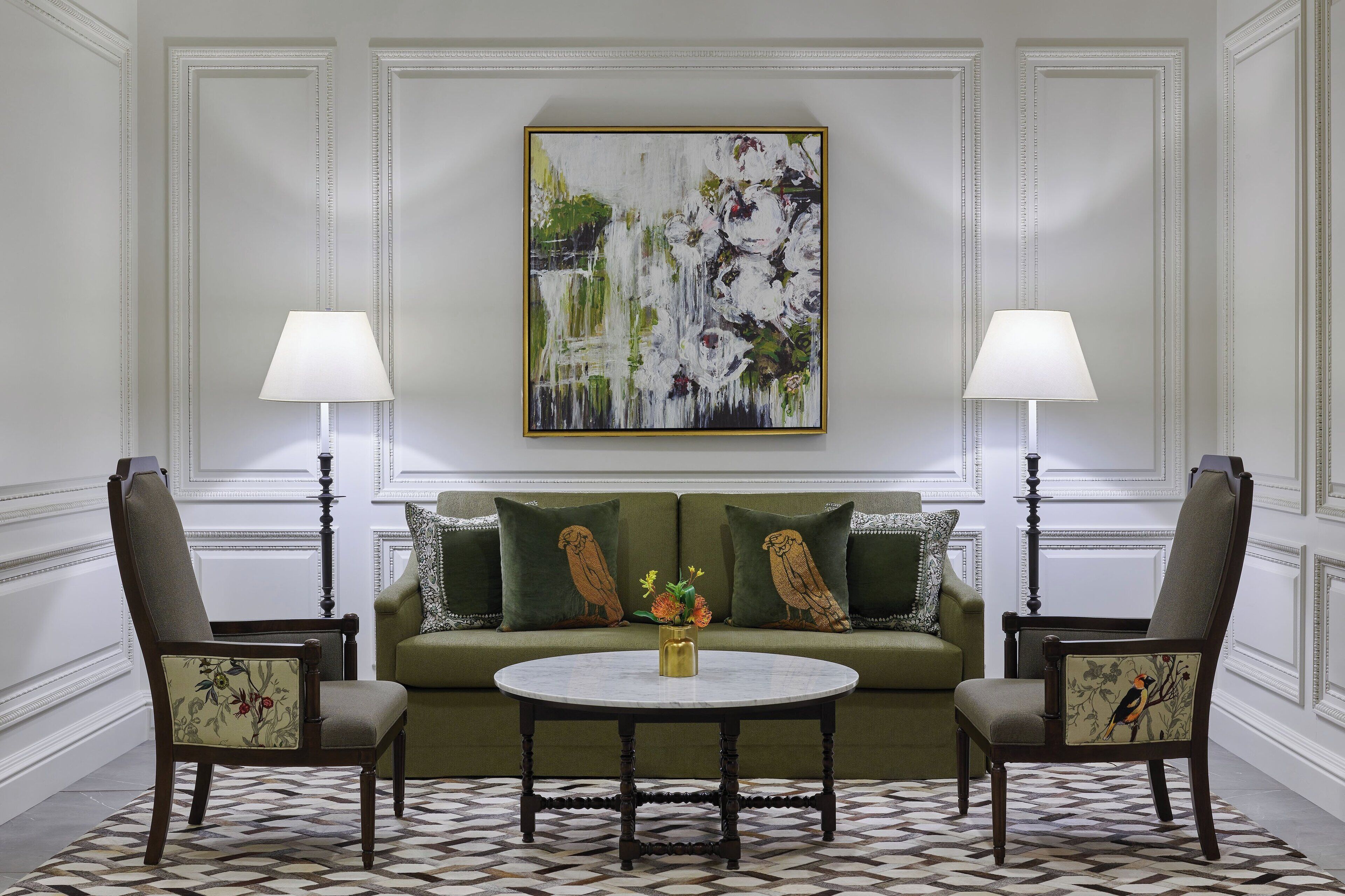 A formal living room with a green sofa, two upholstered chairs, a round coffee table, and a painting above.