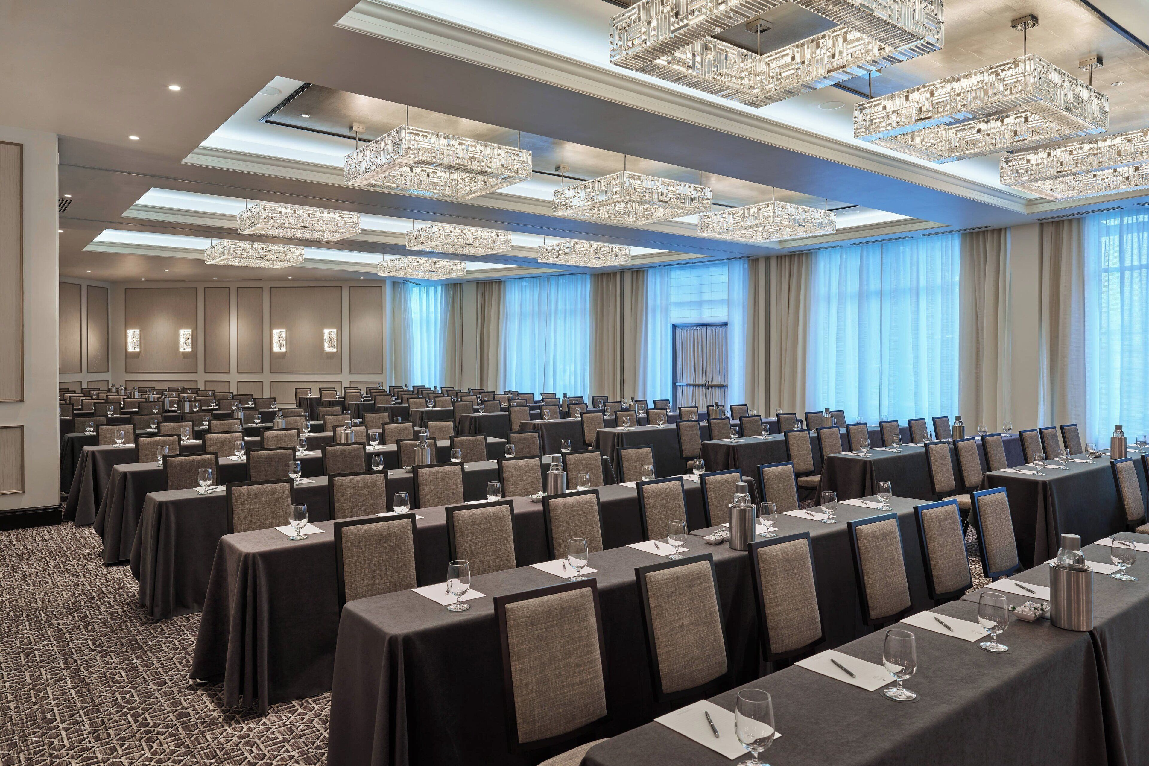 A conference room with rows of tables, chairs, and crystal chandeliers.