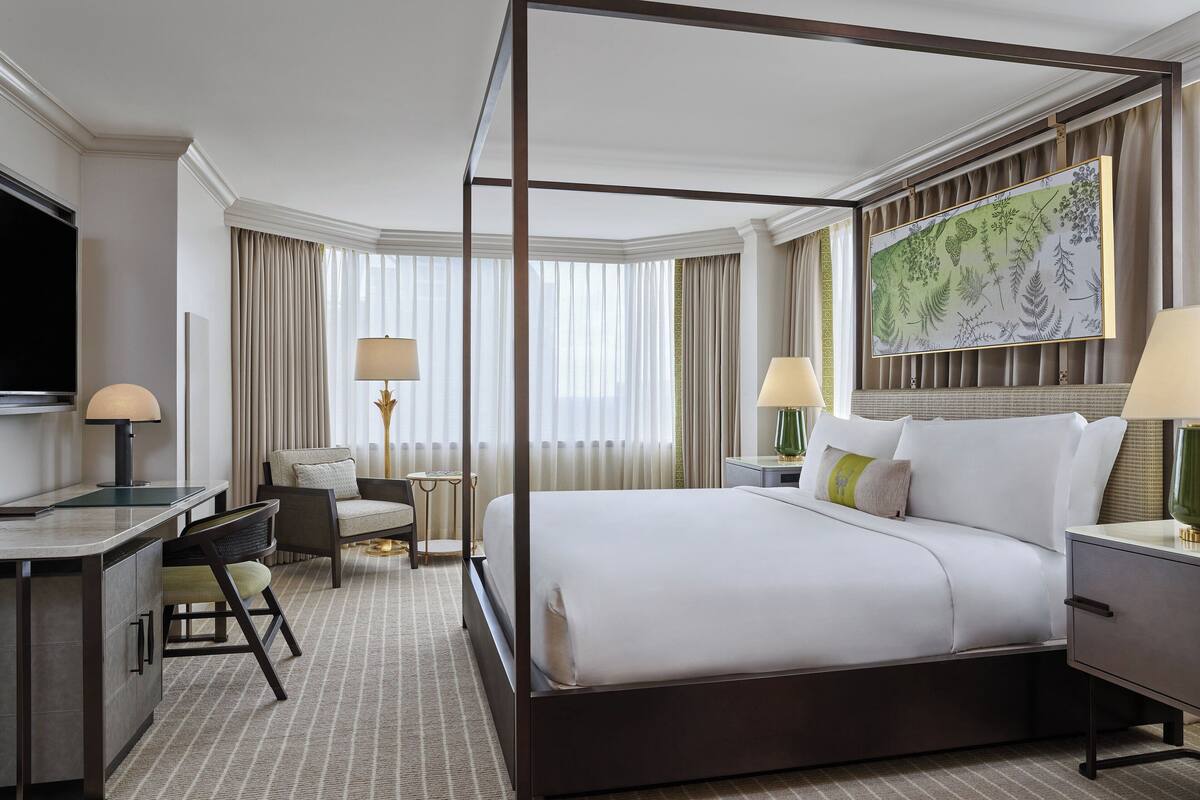 A four-poster bed with a large botanical print on the wall, a desk with a lamp, a chair, and a television.