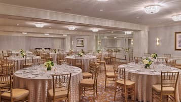 A banquet hall with round tables, gold chairs, and chandeliers.