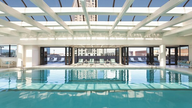 Una grande piscina interna con acqua cristallina e blu, circondata da lettini e un soffitto in vetro.