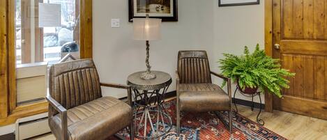 A room with two leather chairs, a small table, a lamp, a patterned rug, and a potted plant.