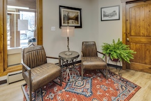 A room with two leather chairs, a small table, a lamp, a patterned rug, and a potted plant.