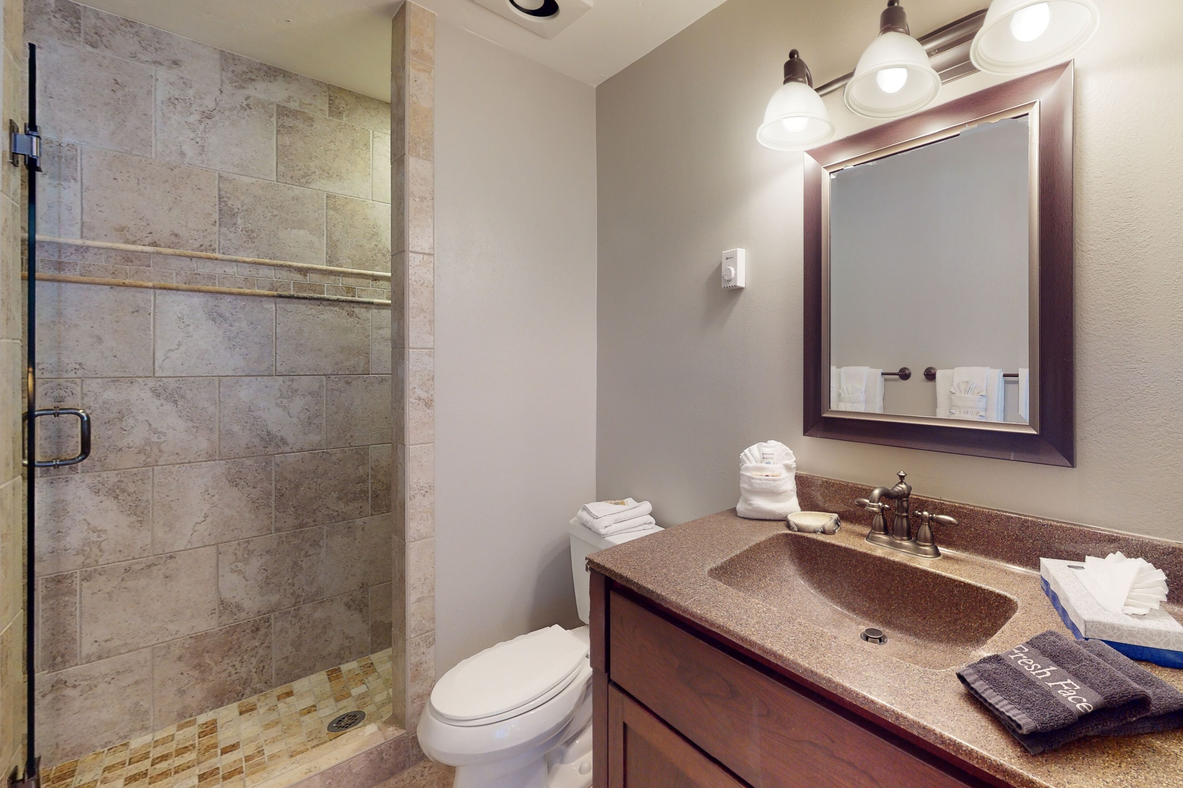 A bathroom with a shower, toilet, sink, and mirror.