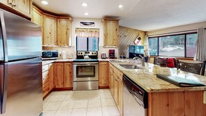 A kitchen with wooden cabinets, stainless steel appliances, a granite countertop, and a window with a view of a snowy landscape. - Pine Ridge Condominiums (Breckenridge)