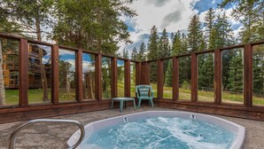 A hot tub with a view of a forest, a wooden deck, and a chair. - Pine Ridge Condominiums (Breckenridge)