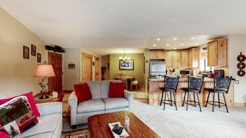 A living room with a sofa, coffee table, and kitchen area with wooden cabinets and bar stools.