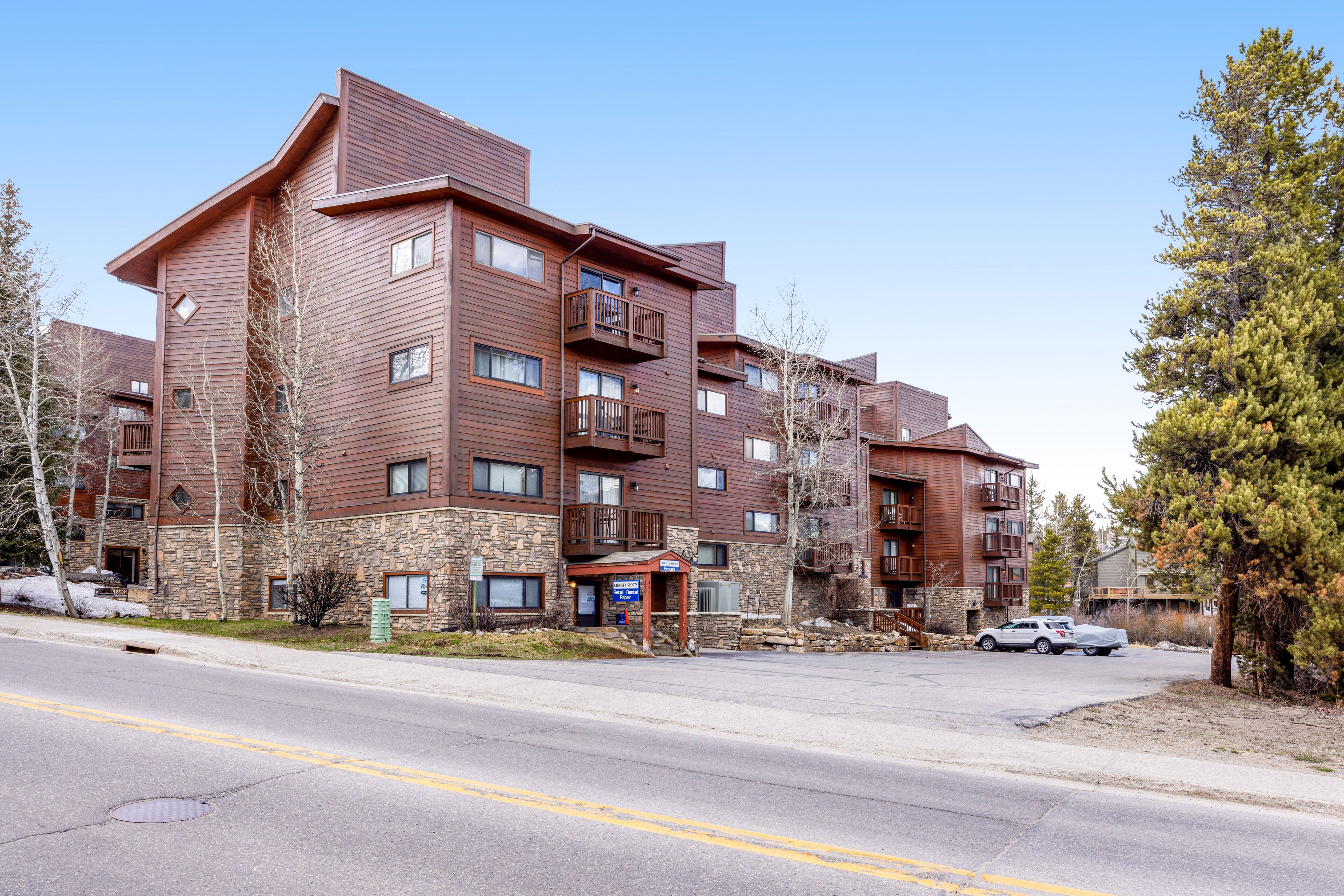 A multi-story building with a stone facade and wooden exterior, featuring balconies and a covered entrance.