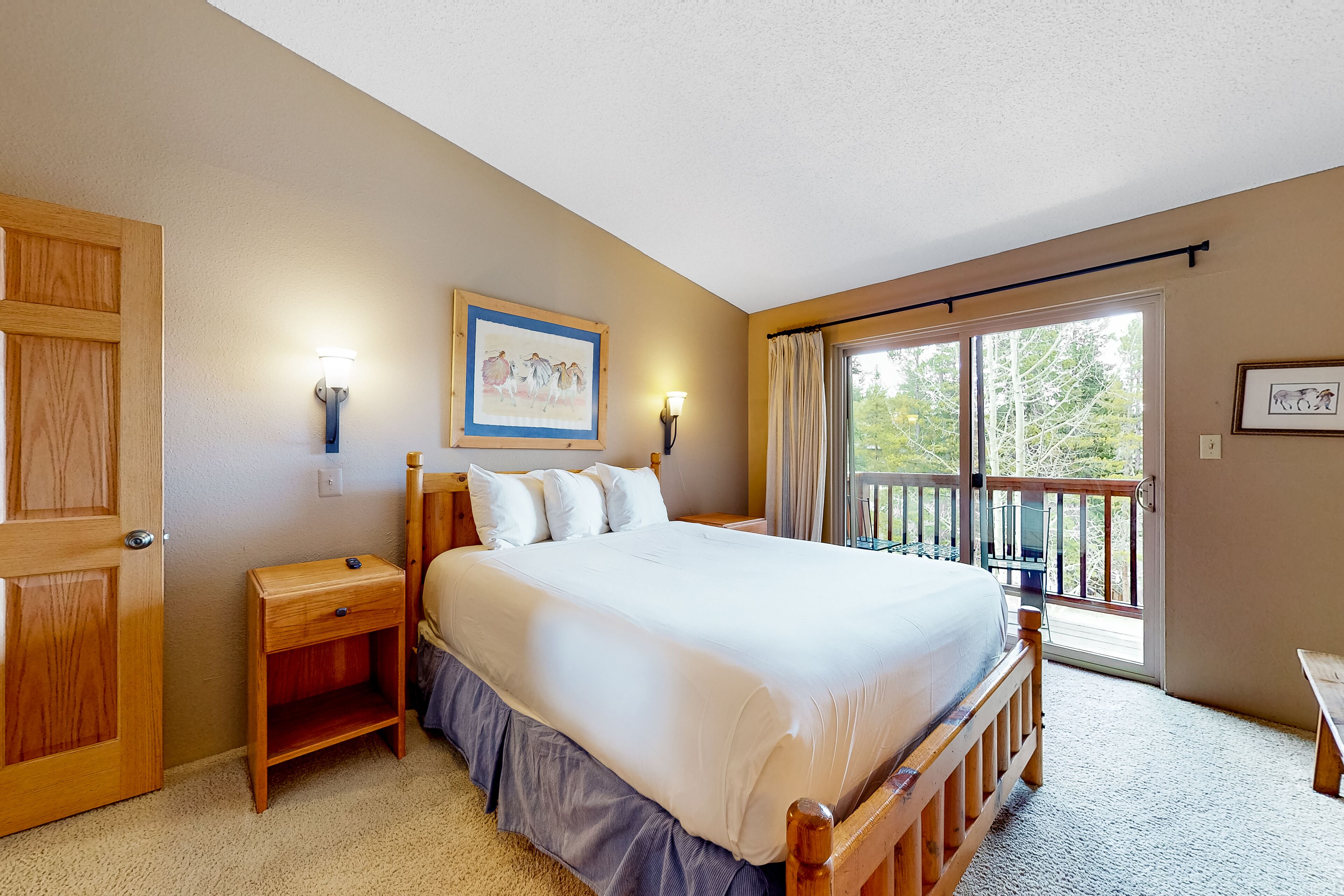 A bedroom with a large bed, wooden headboard, two bedside tables, a nightstand, a window with curtains, and a balcony with a railing.