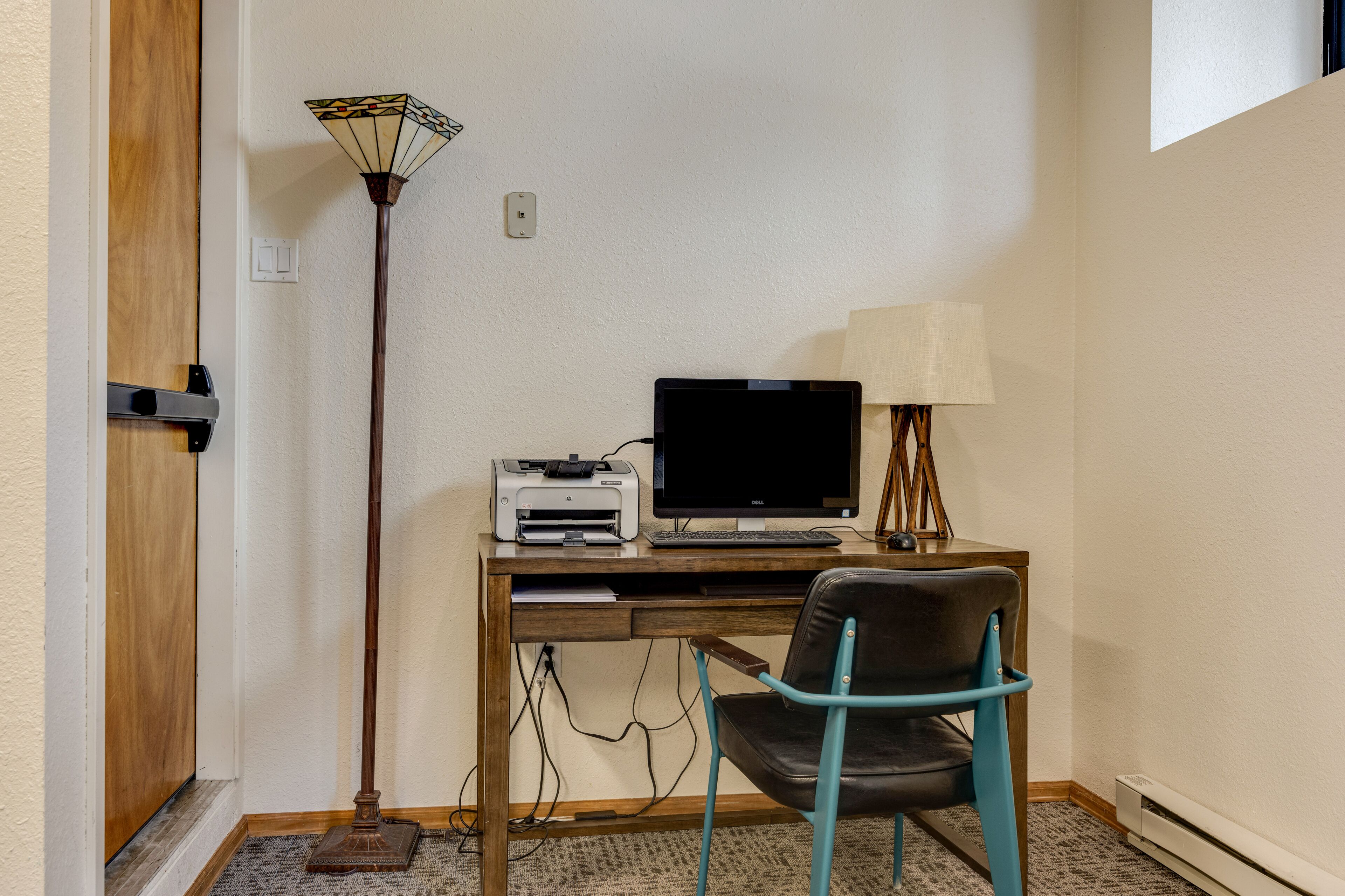 A room with a wooden desk, a computer, a printer, a lamp, and a chair.