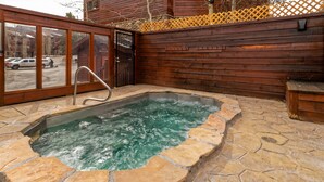 A stone-fenced hot tub area with a wooden deck and a glass door leading to a parking lot. - Pine Ridge Condominiums (Breckenridge)