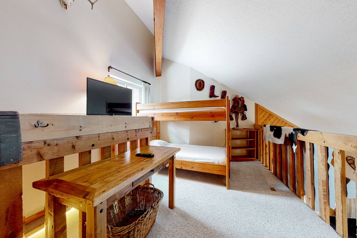 Ein gemütliches Schlafzimmer im Dachgeschoss mit einem Etagenbett, einem hölzernen Schreibtisch, einem Fernseher und einem Fenster mit Vorhängen.