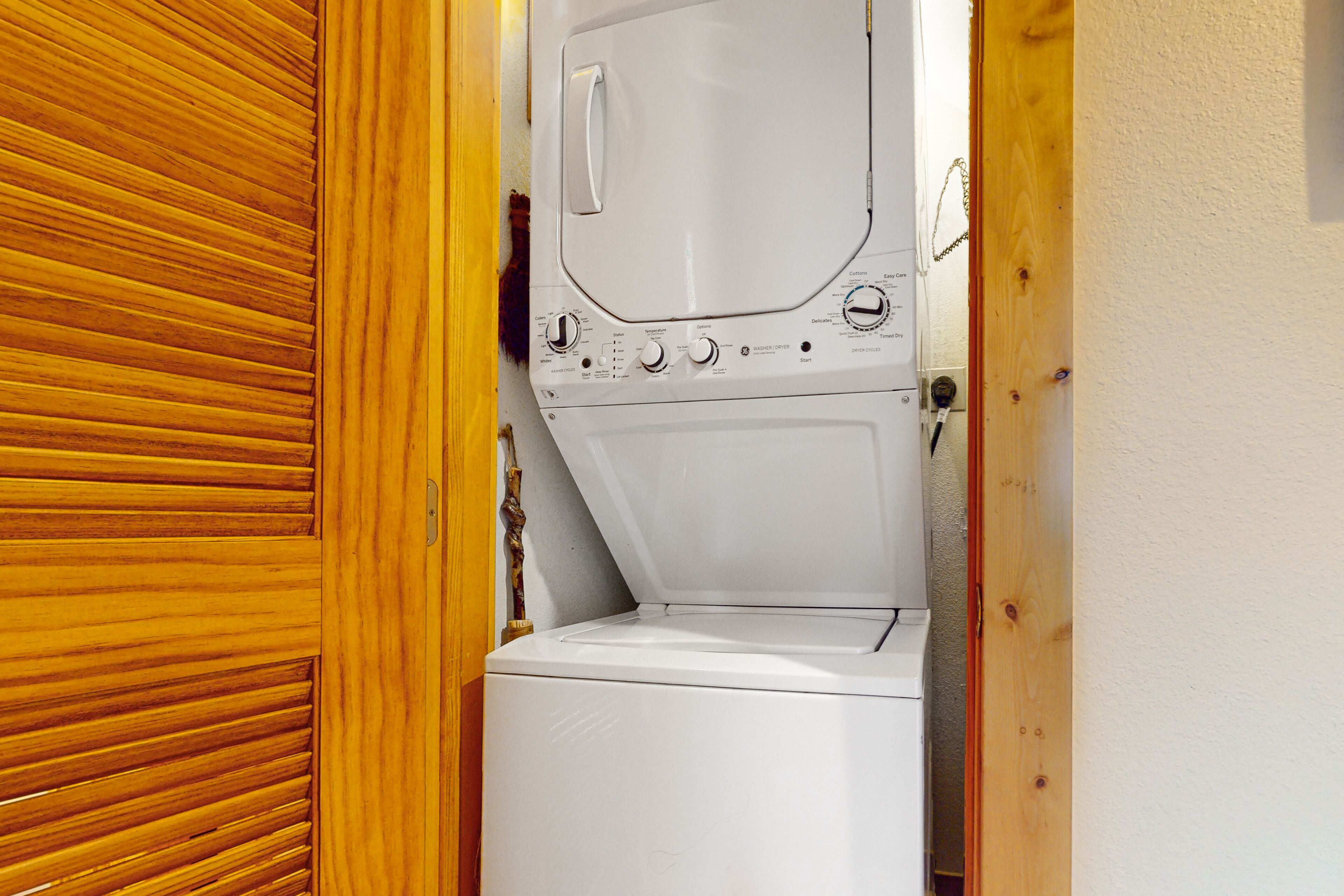 A white washing machine in a small laundry room with wooden paneling on one side.