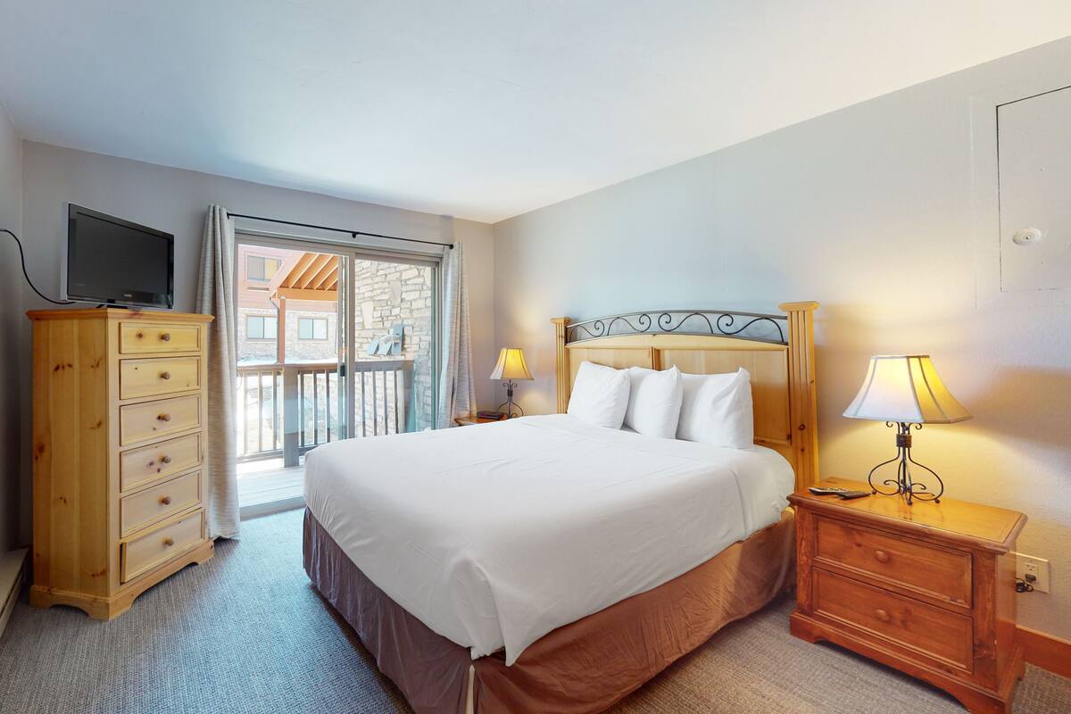 Ein Hotelzimmer mit Bett, Holzschrank, Fernseher und Balkonblick.