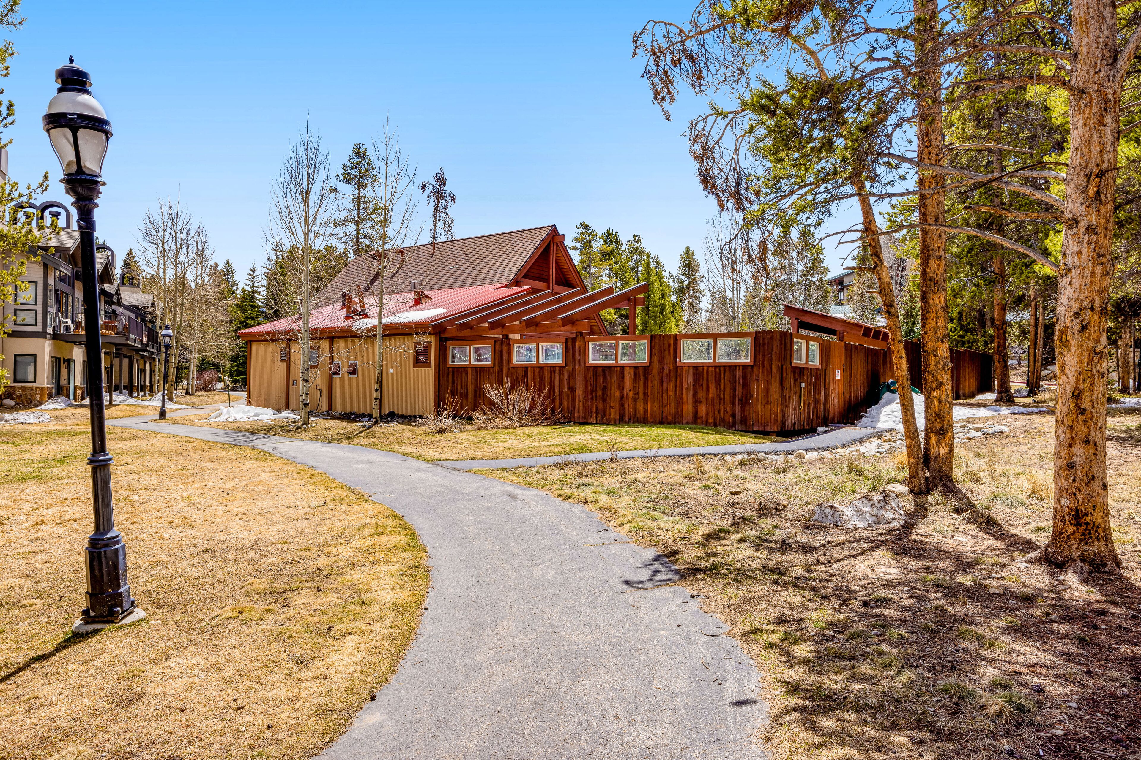A wooden cabin with a metal roof, surrounded by trees and a paved path.