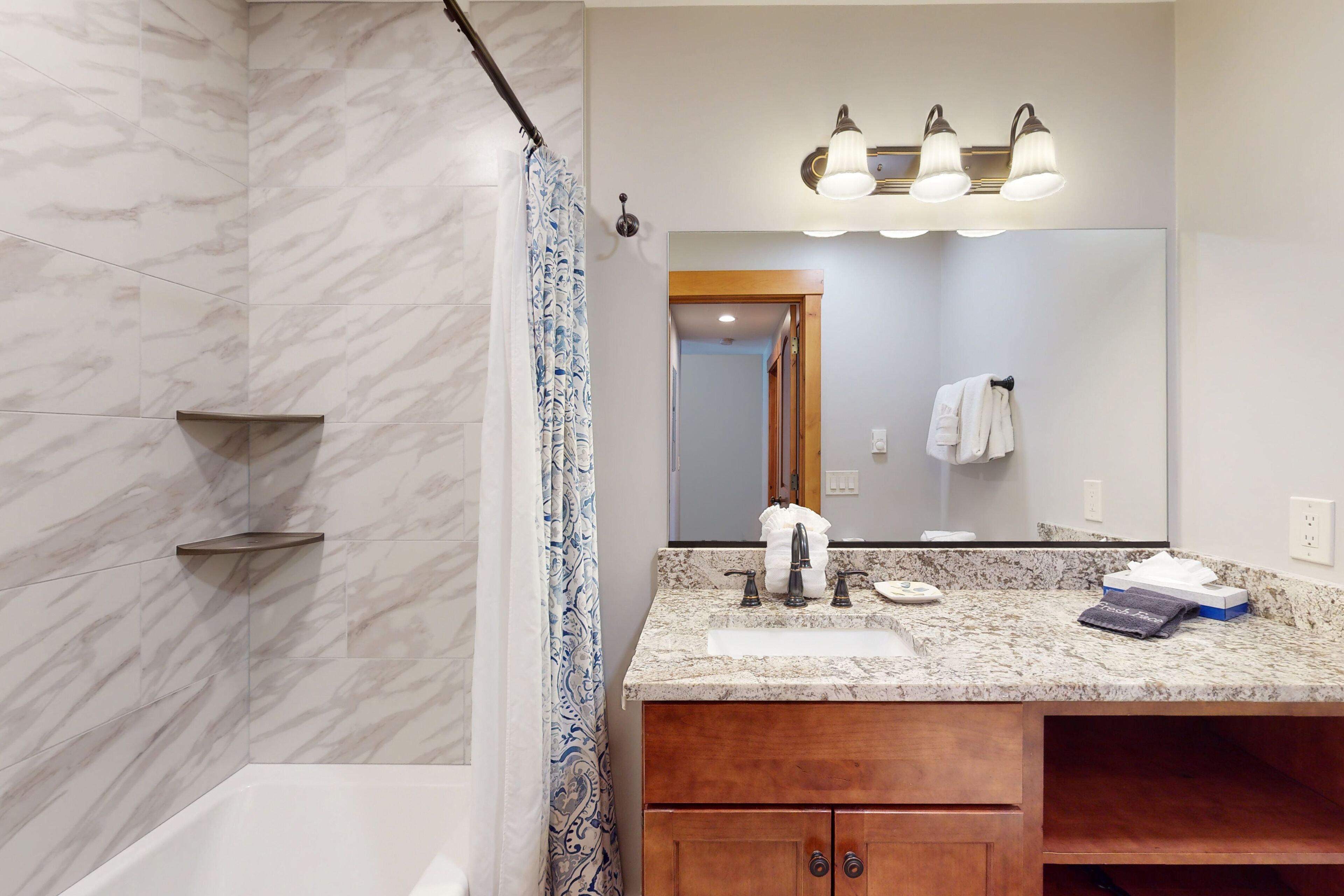 A bathroom with a marble wall, a sink with a mirror above it, and a shower curtain.