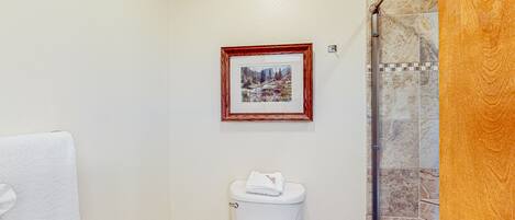 A bathroom with a toilet, a framed picture on the wall, and a shower area.