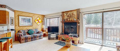 A cozy living room with a sofa, TV, fireplace, and a balcony with a view.