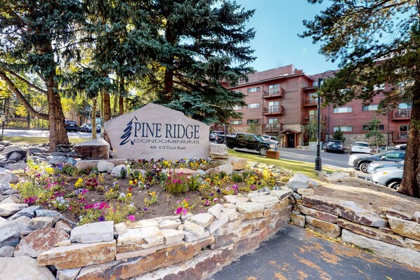 A sign for Pine Ridge Condominiums with a stone wall and flower bed in front.