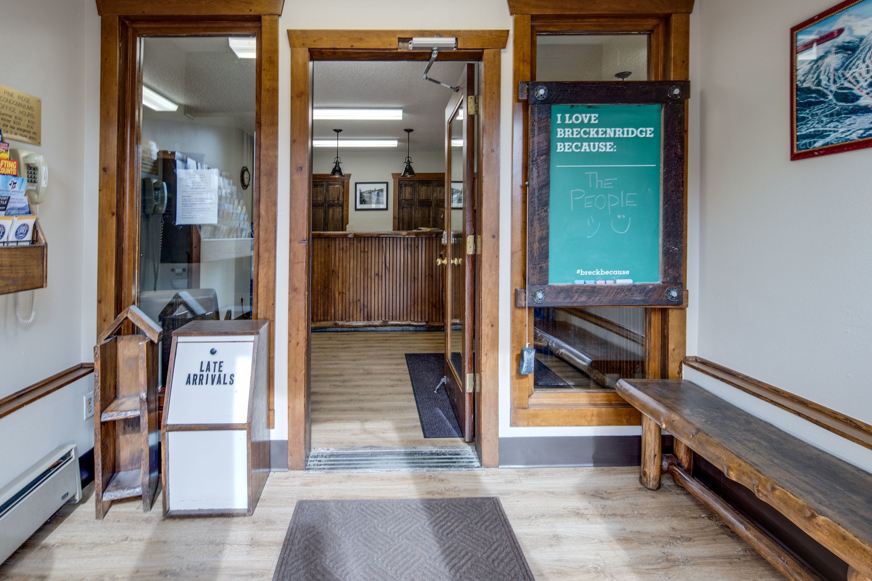 A reception area with a wooden bench, a sign reading "I love Breckenridge because: The People," and a "Late Arrivals" sign.