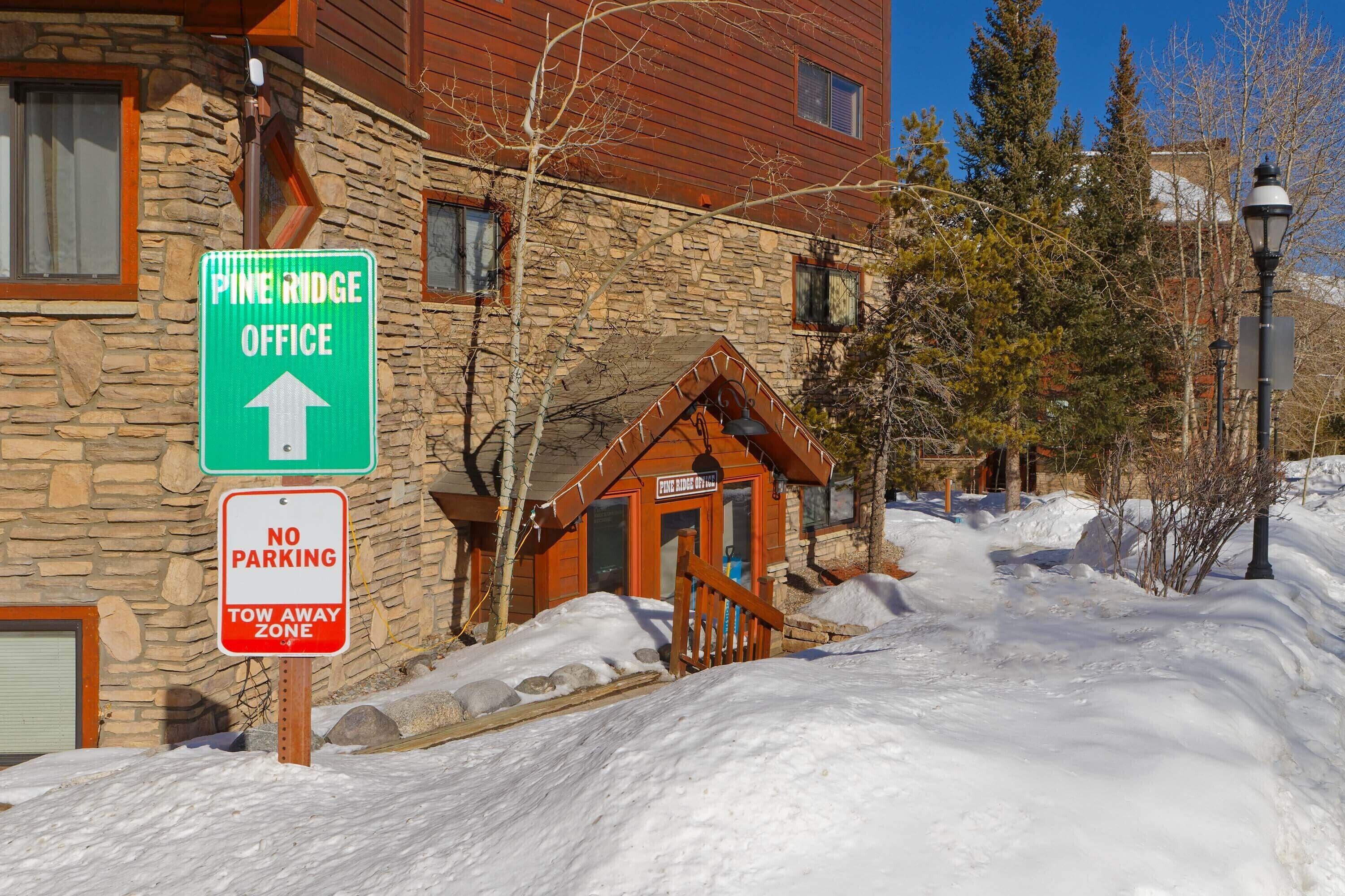A Pine Ridge Office building with a stone facade, wooden entrance, and a 'No Parking' sign.
