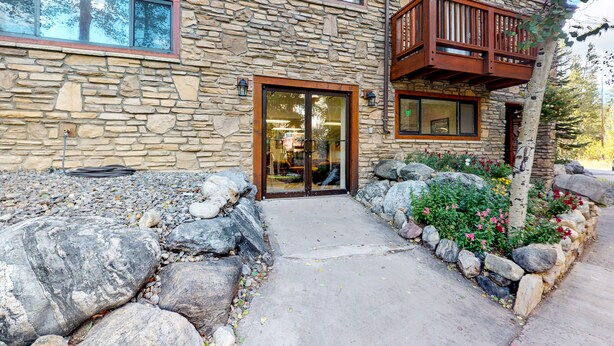 A stone building with a wooden balcony, large windows, and a stone pathway leading to the entrance. - Pine Ridge Condominiums (Breckenridge)