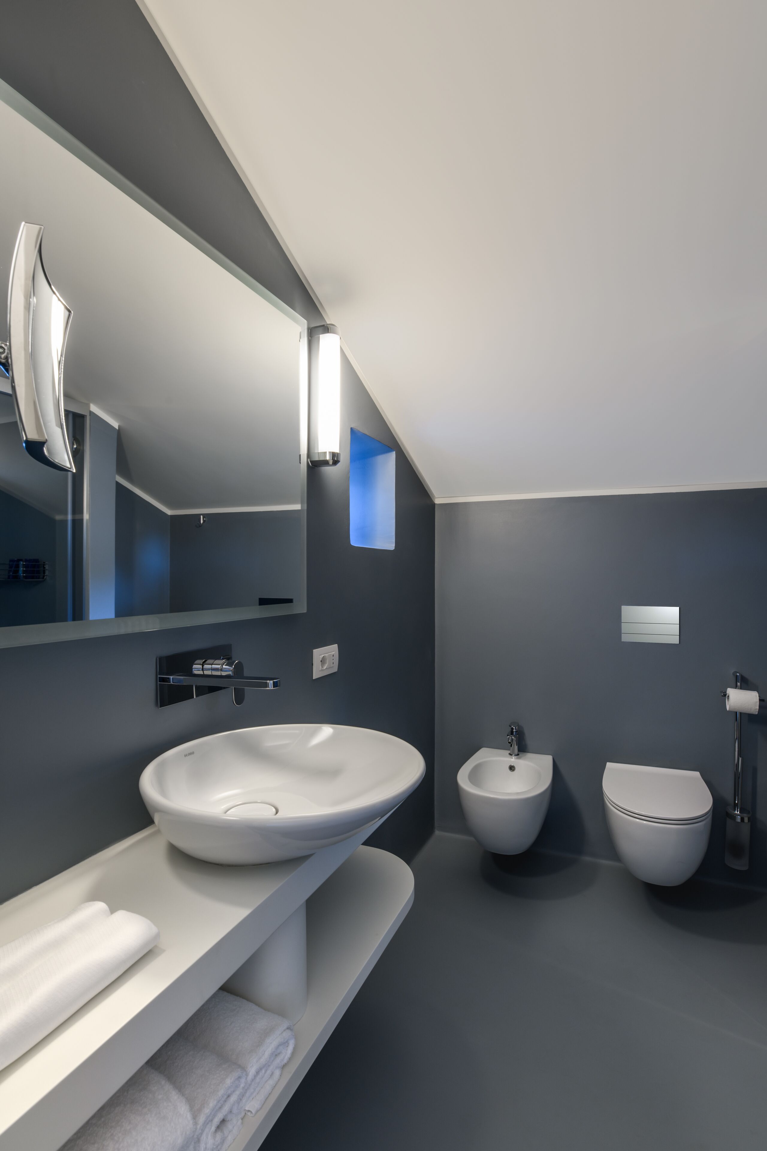 A modern bathroom with a large mirror, a white sink, a bidet, and a toilet.