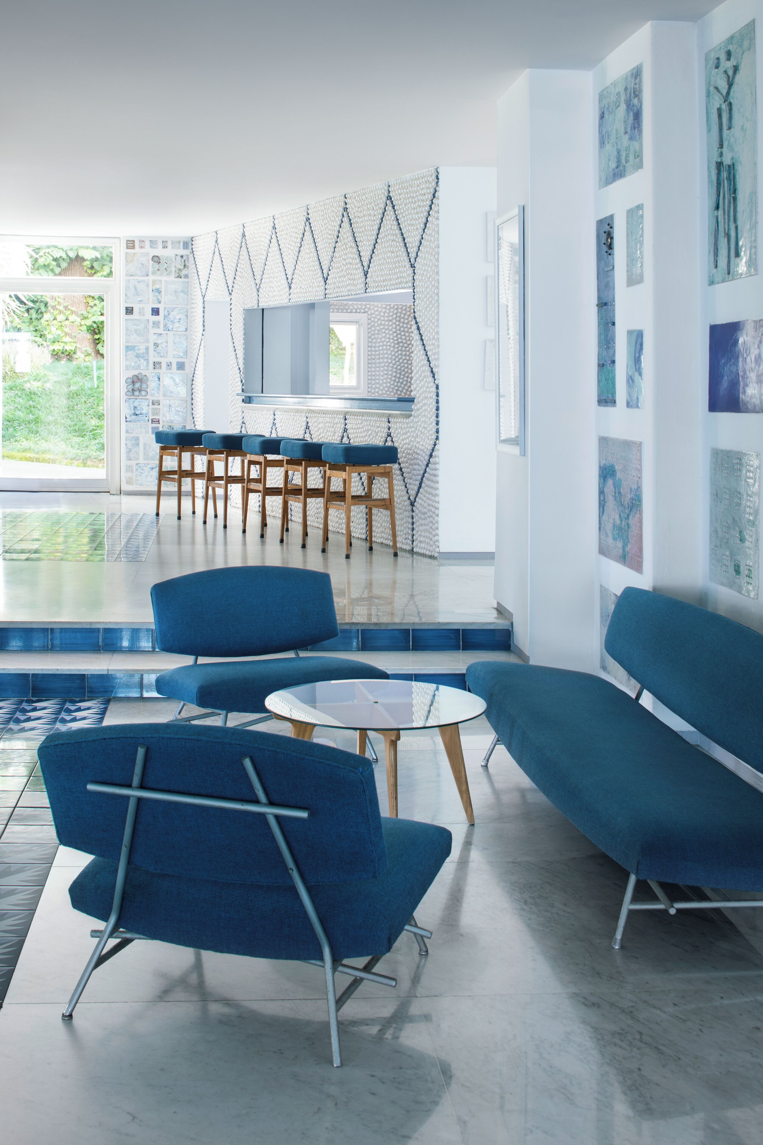 Un soggiorno moderno con mobili blu, un tavolino in vetro e una zona cucina con sedie in legno.