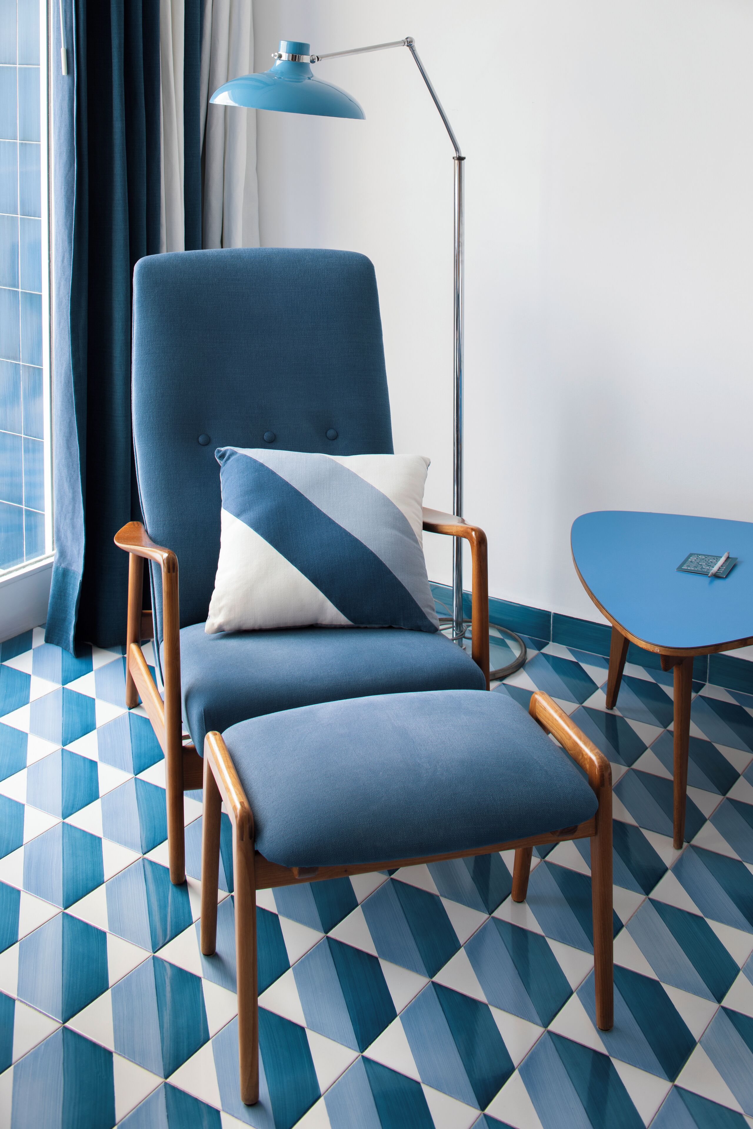 Una habitación moderna con un sillón azul, una mesita y una lámpara de pie.