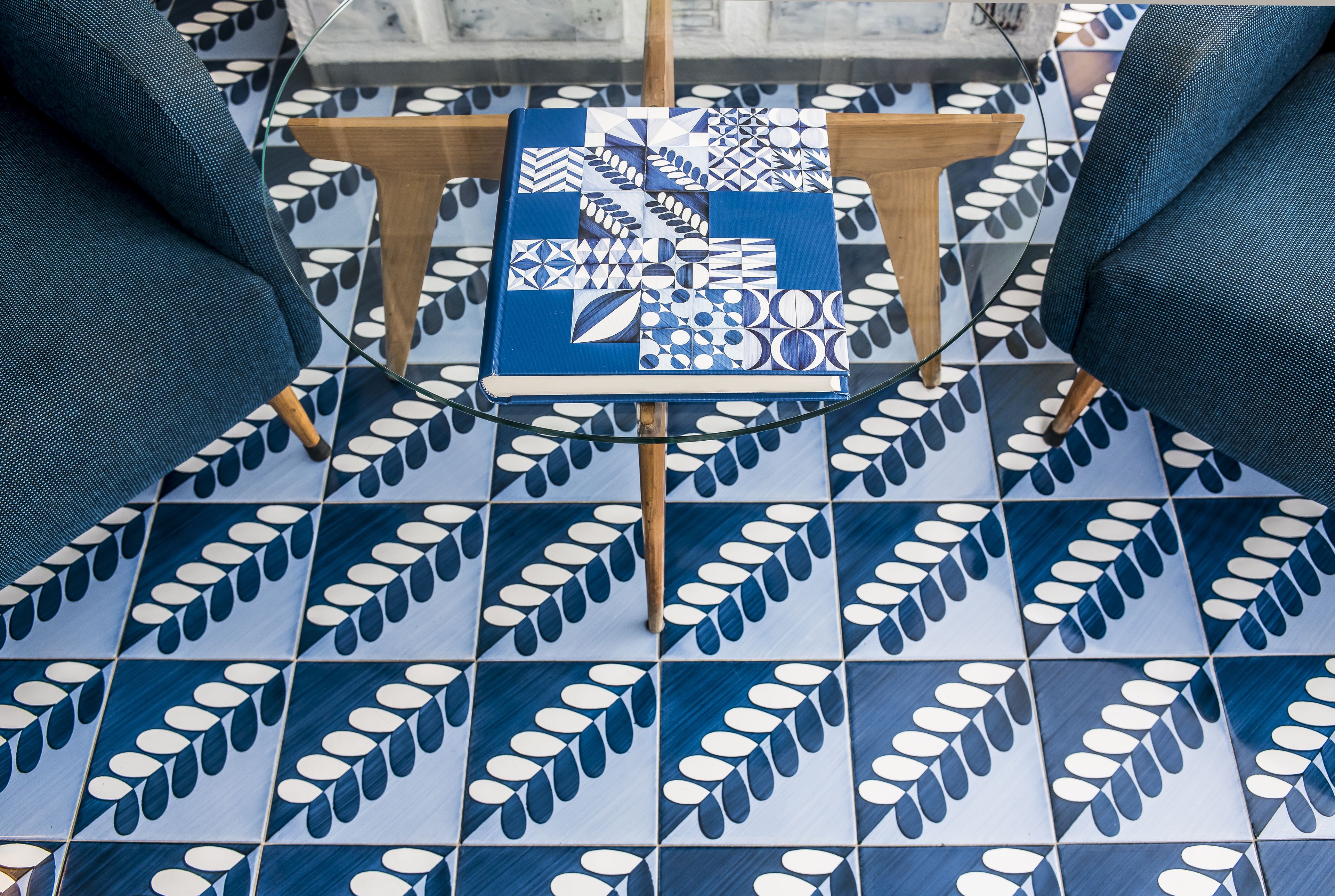 A room with a patterned floor, a glass table, and two blue armchairs.