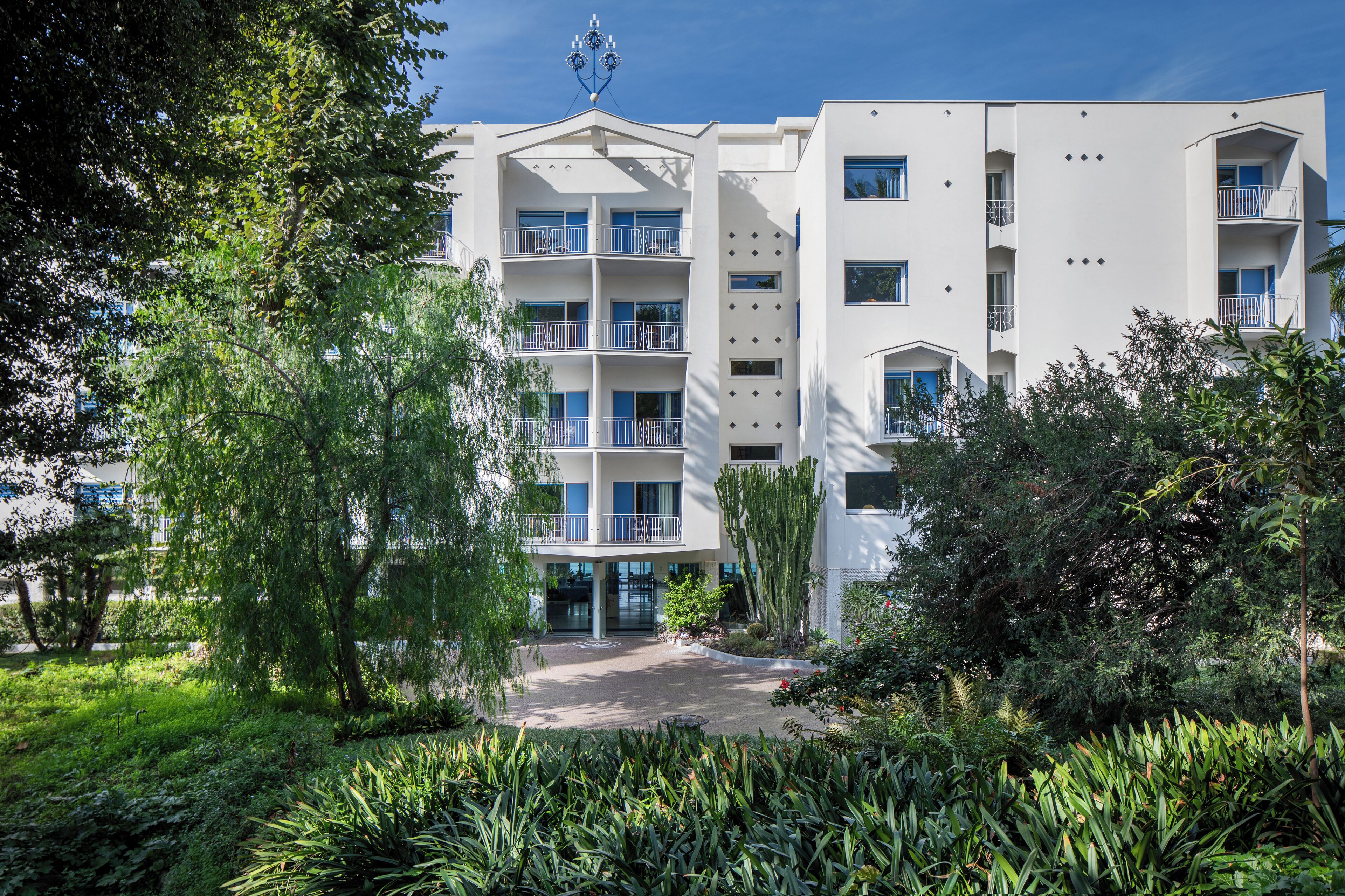 A multi-story building with balconies, surrounded by lush greenery and trees.