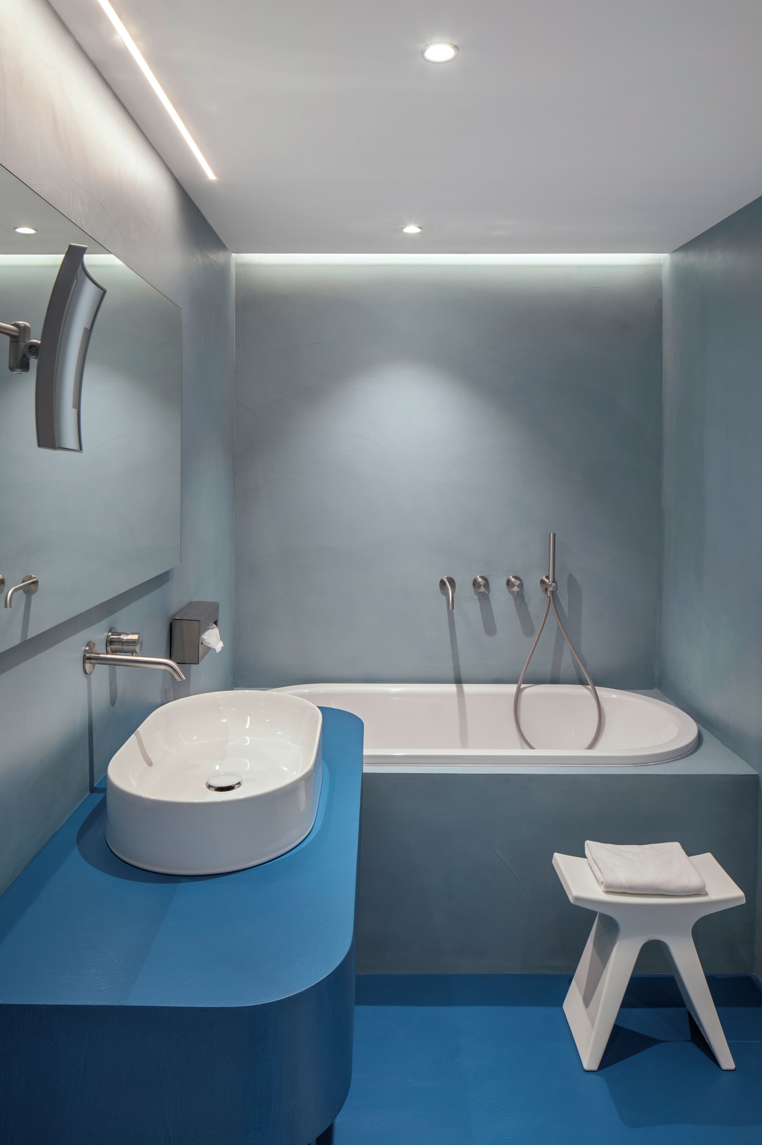 Un bagno moderno con una vasca da bagno bianca, un mobile lavabo blu e un piccolo sgabello bianco.