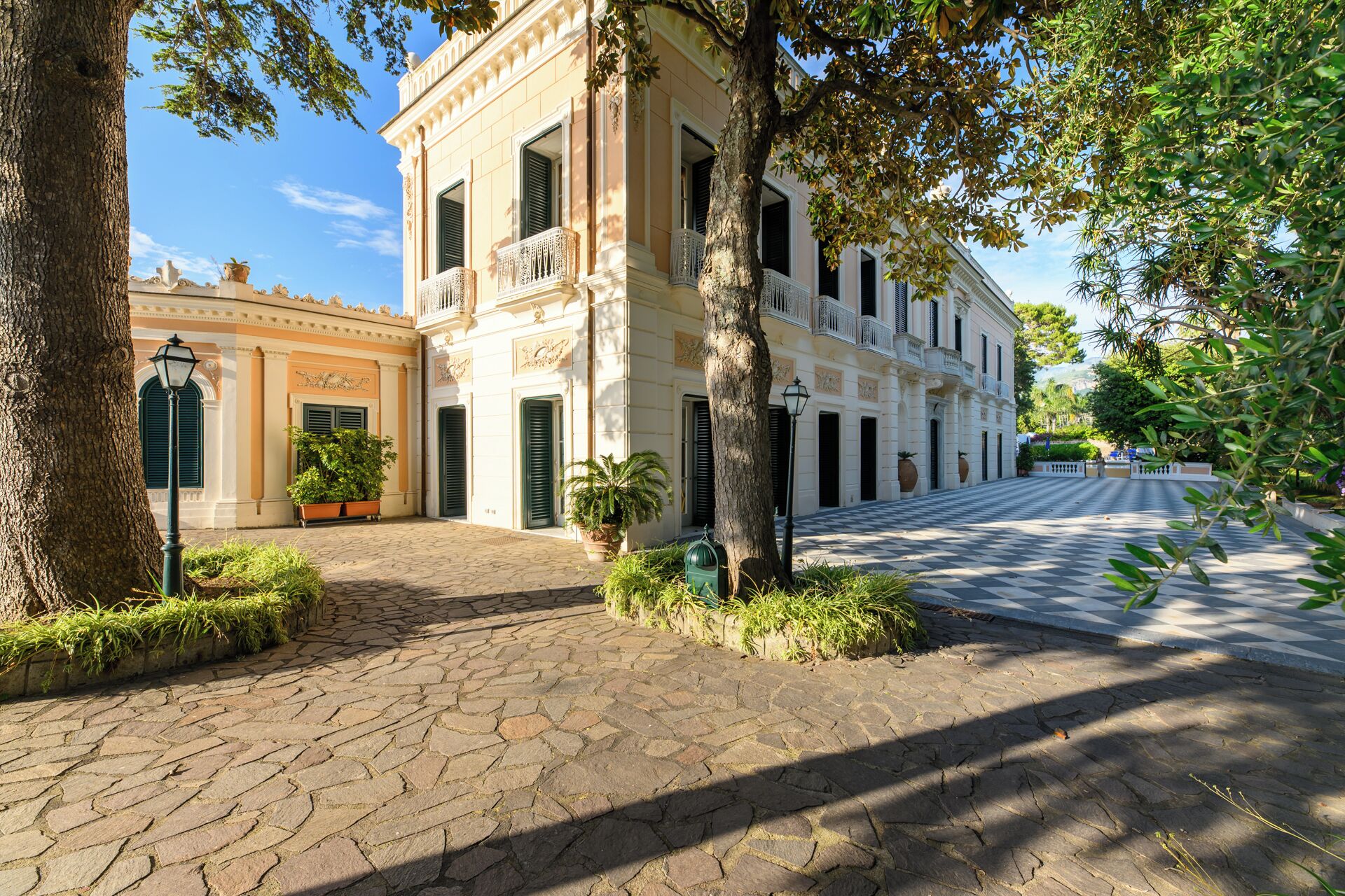 A historic building with a courtyard, stone paving, and mature trees.