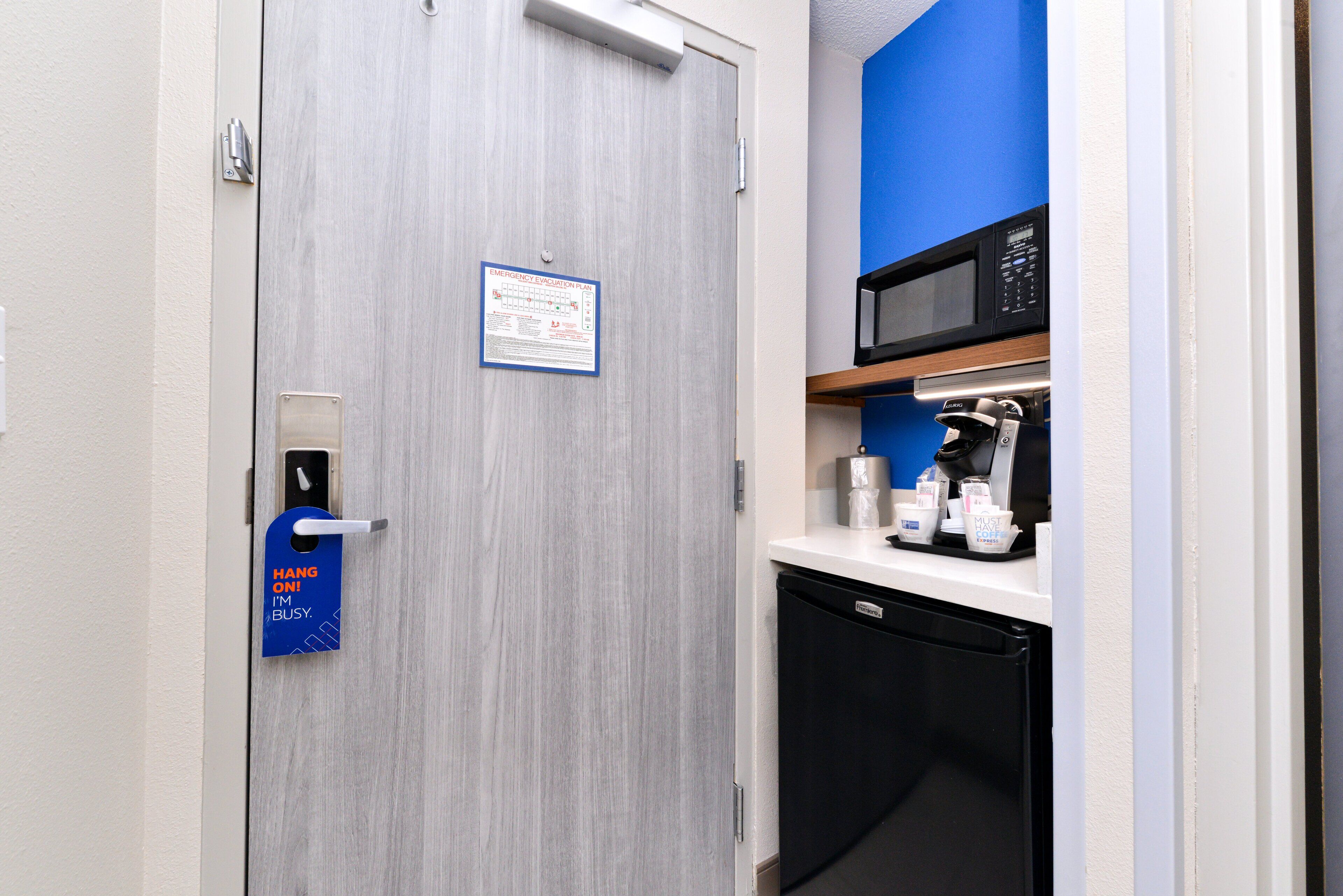Une chambre d’hôtel avec une porte en bois, un mur bleu, un four à micro-ondes, une machine à café et un petit réfrigérateur.