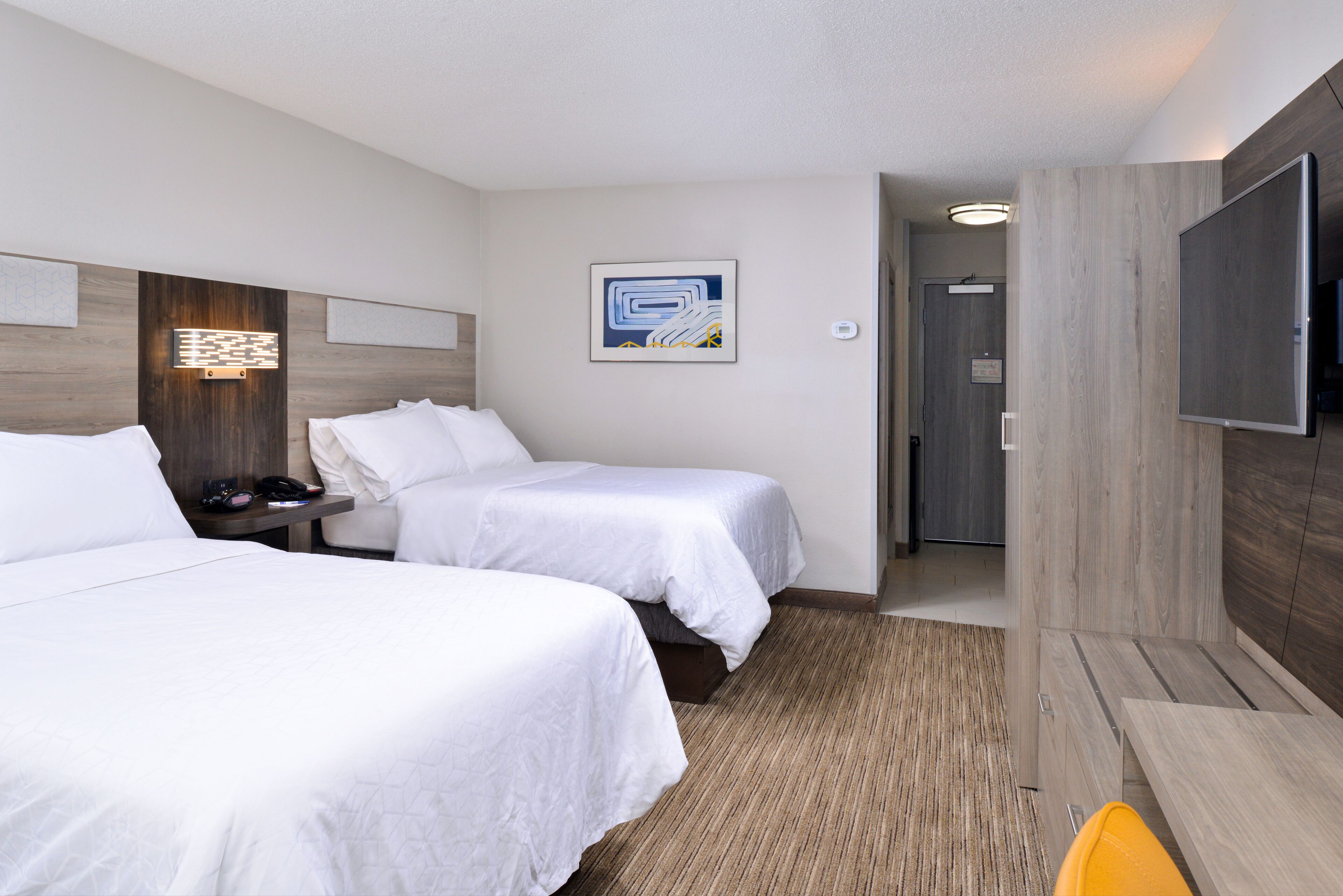 A hotel room with two beds, a flat-screen TV, a bedside table, and a wall-mounted artwork.