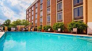 A swimming pool with lounge chairs and a brick building in the background. - Holiday Inn Express Winston-Salem Medical Center Area by IHG (Winston-Salem)