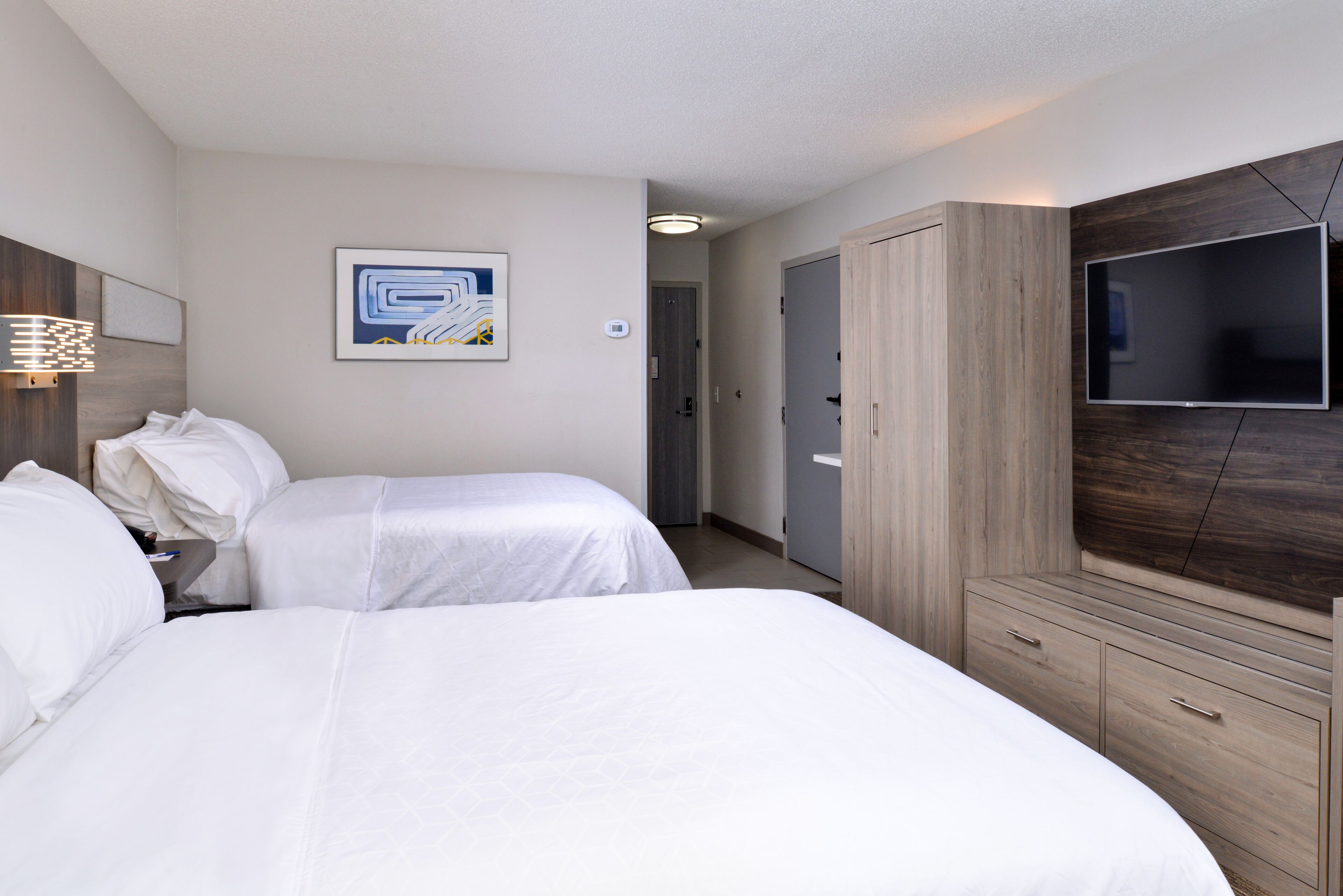 Una habitación de hotel con dos camas, un televisor, un armario y un cuadro en la pared.
