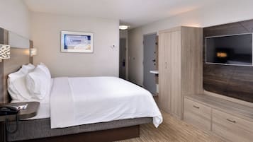 Ein Hotelzimmer mit Bett, Nachttisch, Lampe, Fernseher, Kleiderschrank und einem Bild an der Wand.
