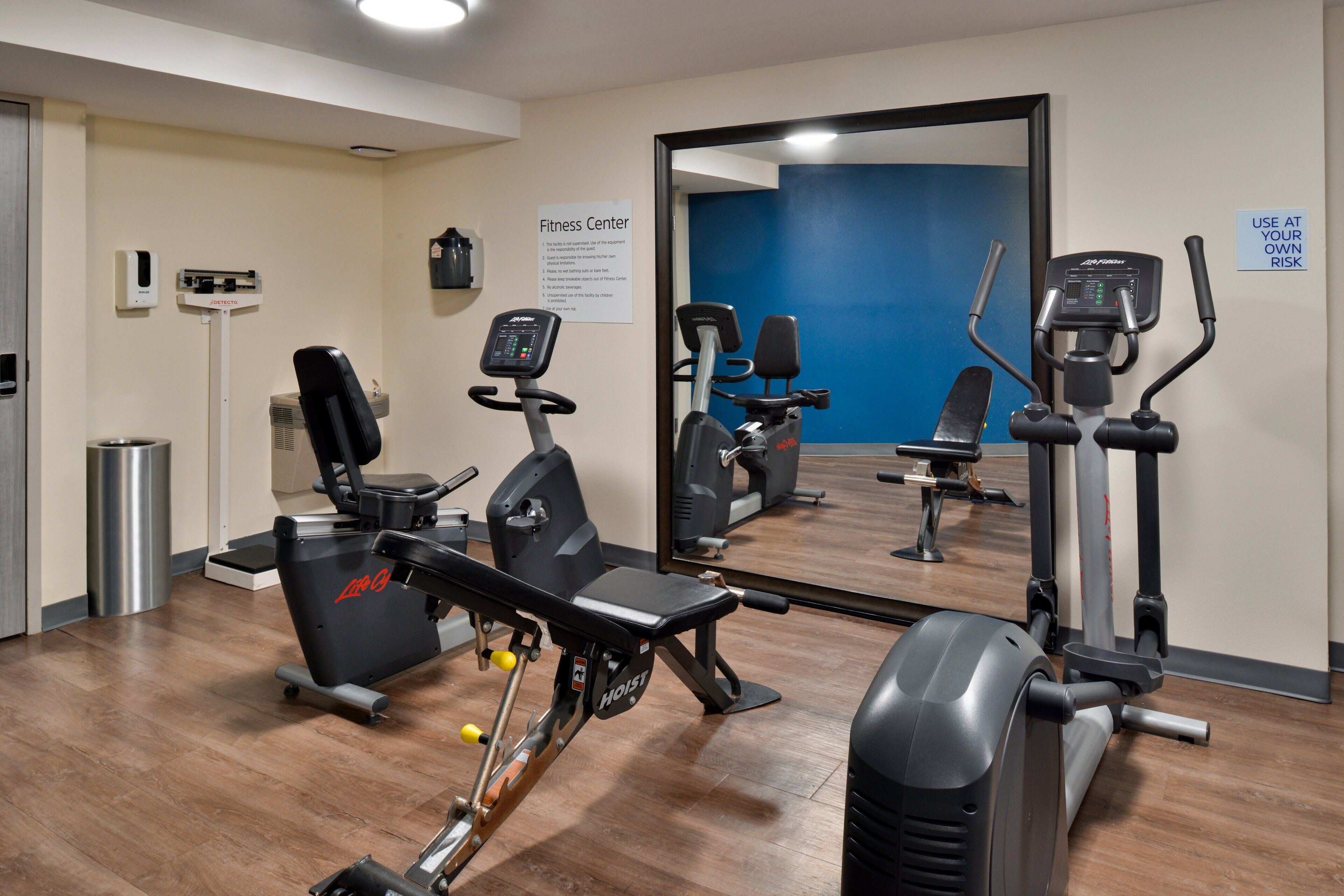 A fitness center with cardio machines, a weight bench, and a mirror reflecting the equipment.