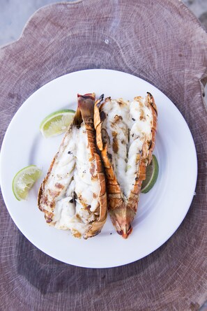 A plate with grilled lobster meat and lime wedges. - Small Hope Bay Lodge (Andros Town)
