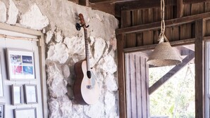 A cozy room with a stone wall, a guitar, a stack of books, a white sofa, and a small table with a bowl of wood. - Small Hope Bay Lodge  (Andros Town)