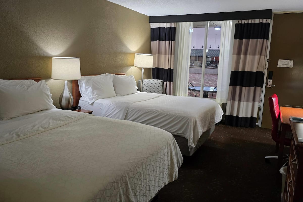 A hotel room with two beds, a desk, a chair, and a view of the outside.