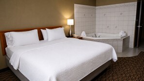 A hotel room with a large bed, a separate bathroom with a bathtub, and a nightstand with a lamp.