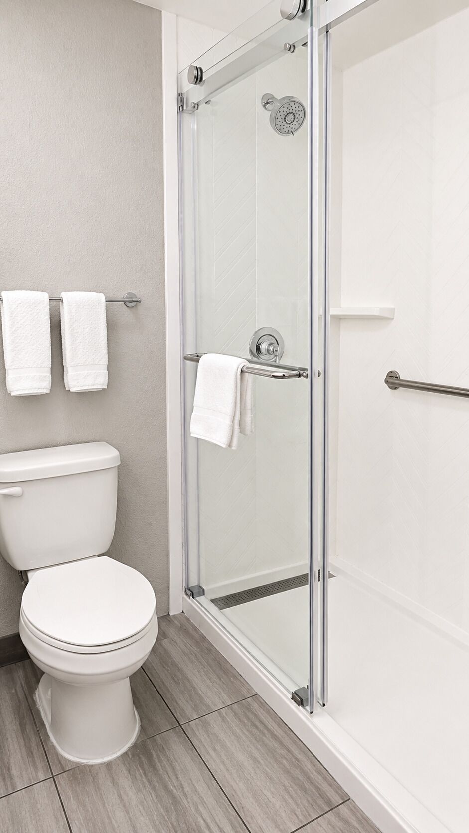 A modern bathroom with a glass-enclosed shower, a toilet, and two towels hanging on a rack.