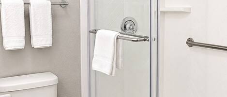 A modern bathroom with a glass-enclosed shower, a toilet, and two towels hanging on a rack.