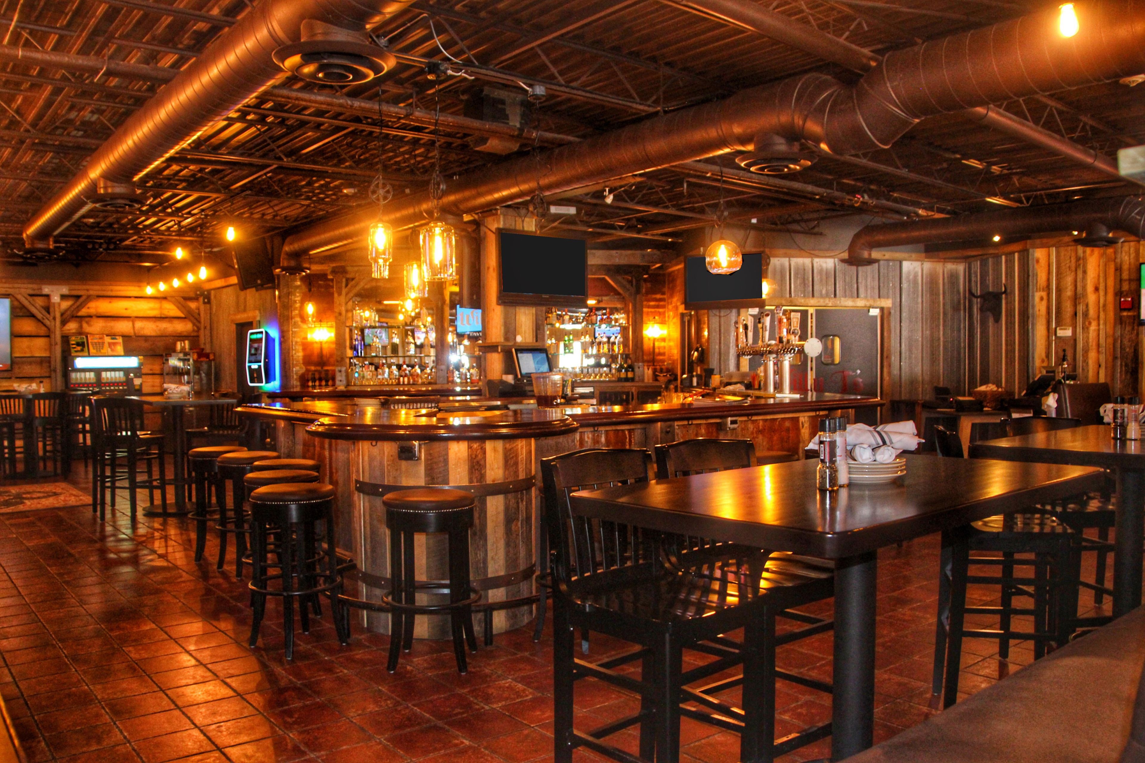 Un área de bar con mesas y taburetes de madera, una barra y lámparas colgantes.
